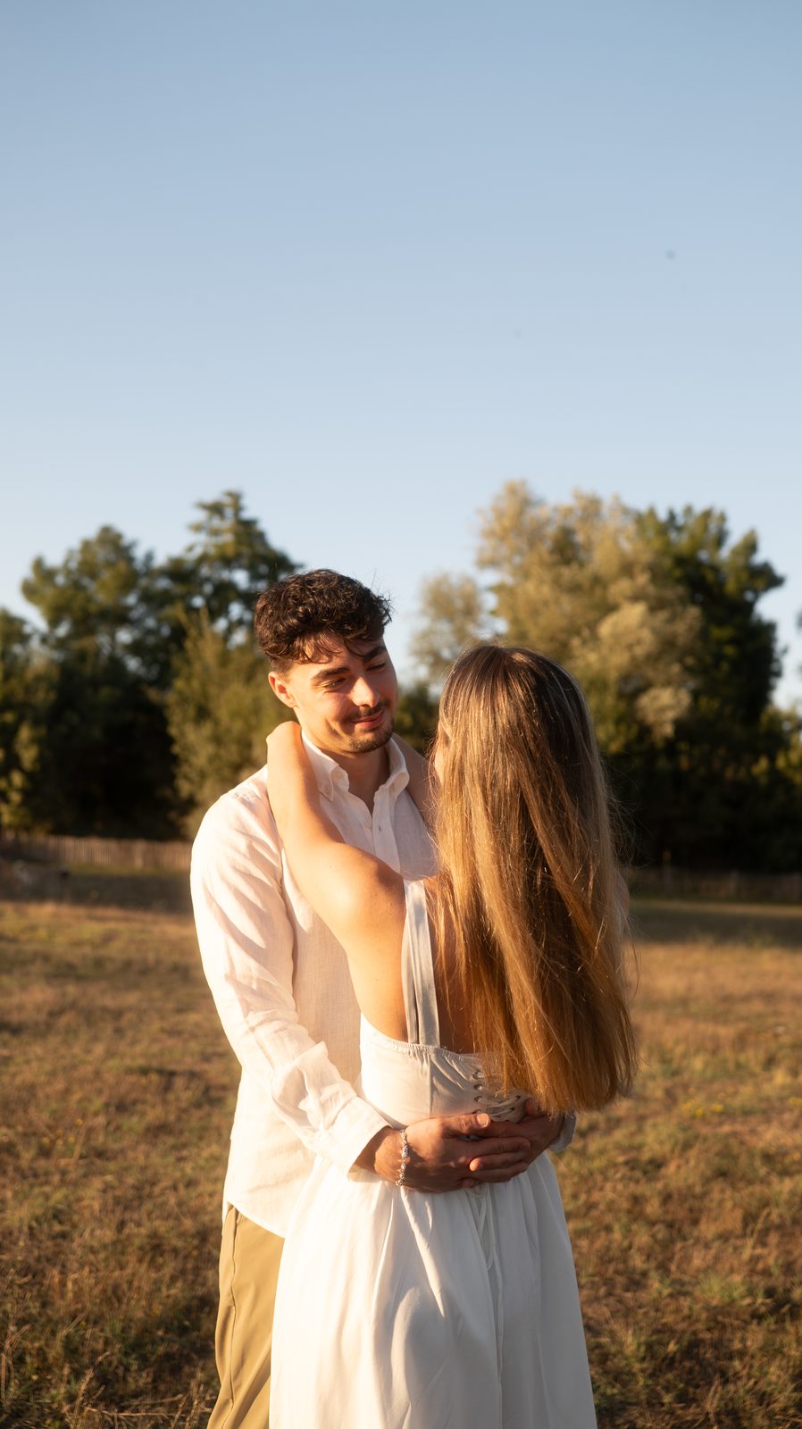 Manon et Benjamin enlacés, les arbres et le ciel derrière eux.