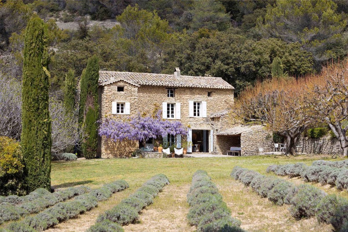 Un mas provençal en pierre sèche, volets clairs et glycine en fleur, entre les cyprès et les rangs de lavande.